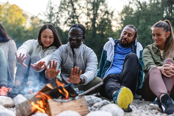 A diverse group of peers enjoying time around a campfire outdoors