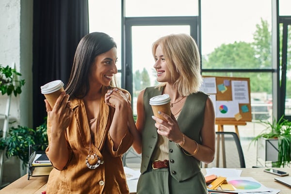 Two women in an office environment smiling and holding coffee