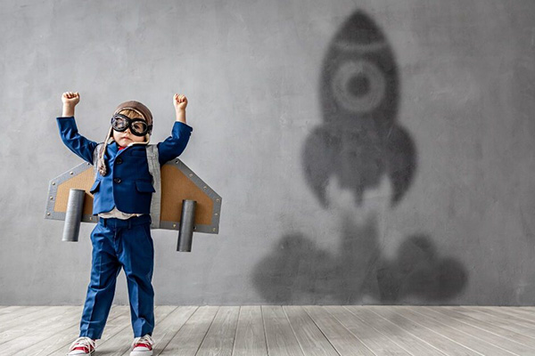 Child dressed as a pilot wearing wings standing in front of wall showing a shadow of a rocket lifting off