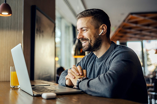 A man sitting at a table, smiling at his laptop