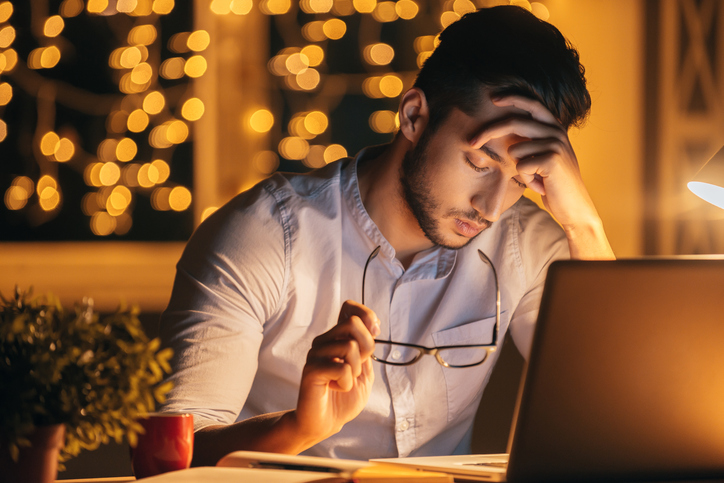 Stressed man looking at laptop with holiday decorations in the background