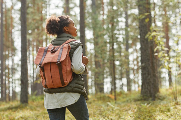 A woman walking in the woods wearing a backback