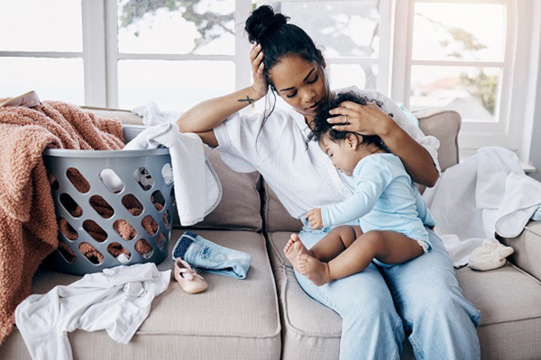 A woman on a couch with a small child on her lap and a laundry basket next to her